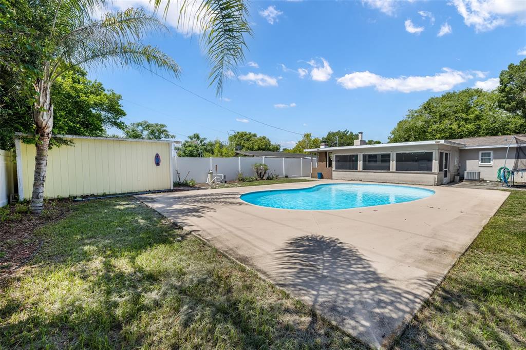 A backyard features a swimming pool, concrete patio, yellow shed, and a white privacy fence — 1509 PRIMROSE LANE, DAYTONA BEACH, FL