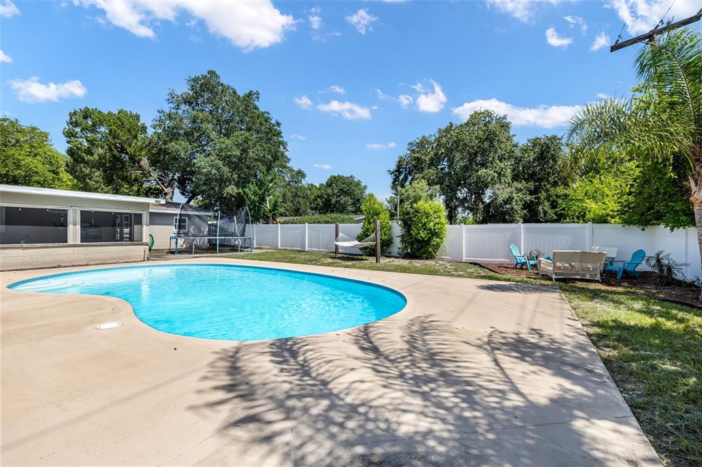 A backyard features a swimming pool, concrete patio, white vinyl fence, and mature trees — 1509 PRIMROSE LANE, DAYTONA BEACH, FL