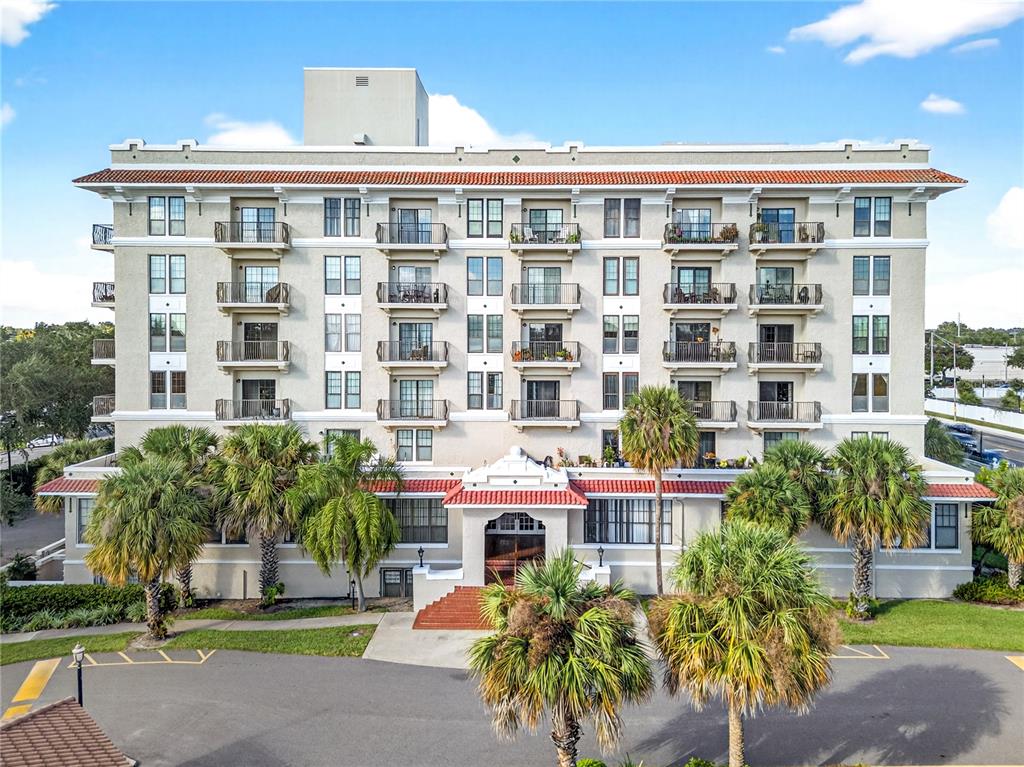 A multi-story building with balconies and a red tile roof sits above a parking lot — 235 6TH STREET NW UNIT 307, WINTER HAVEN, FL