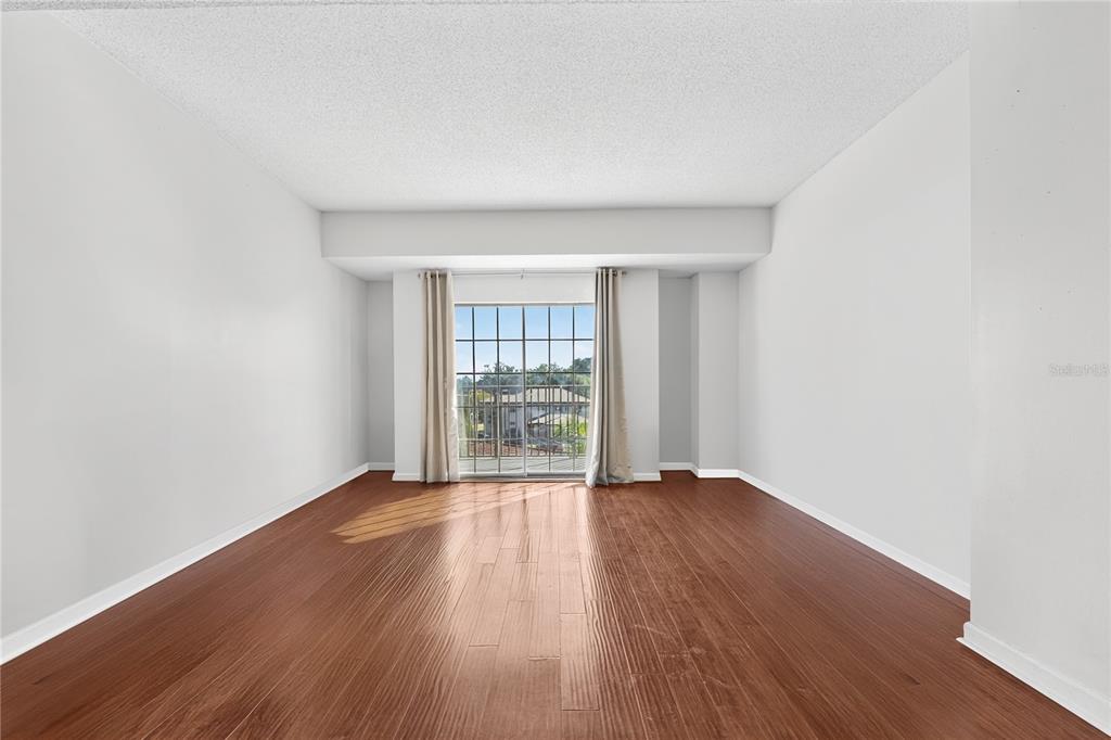 An empty room with wood-look flooring, white walls, and a sliding glass door to a balcony — 235 6TH STREET NW UNIT 307, WINTER HAVEN, FL