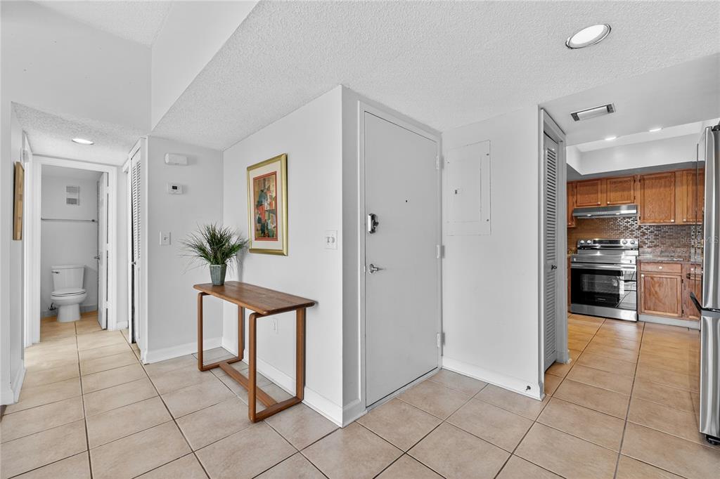 A tiled entryway features a wooden console table, a white door, and a nearby kitchen — 235 6TH STREET NW UNIT 307, WINTER HAVEN, FL