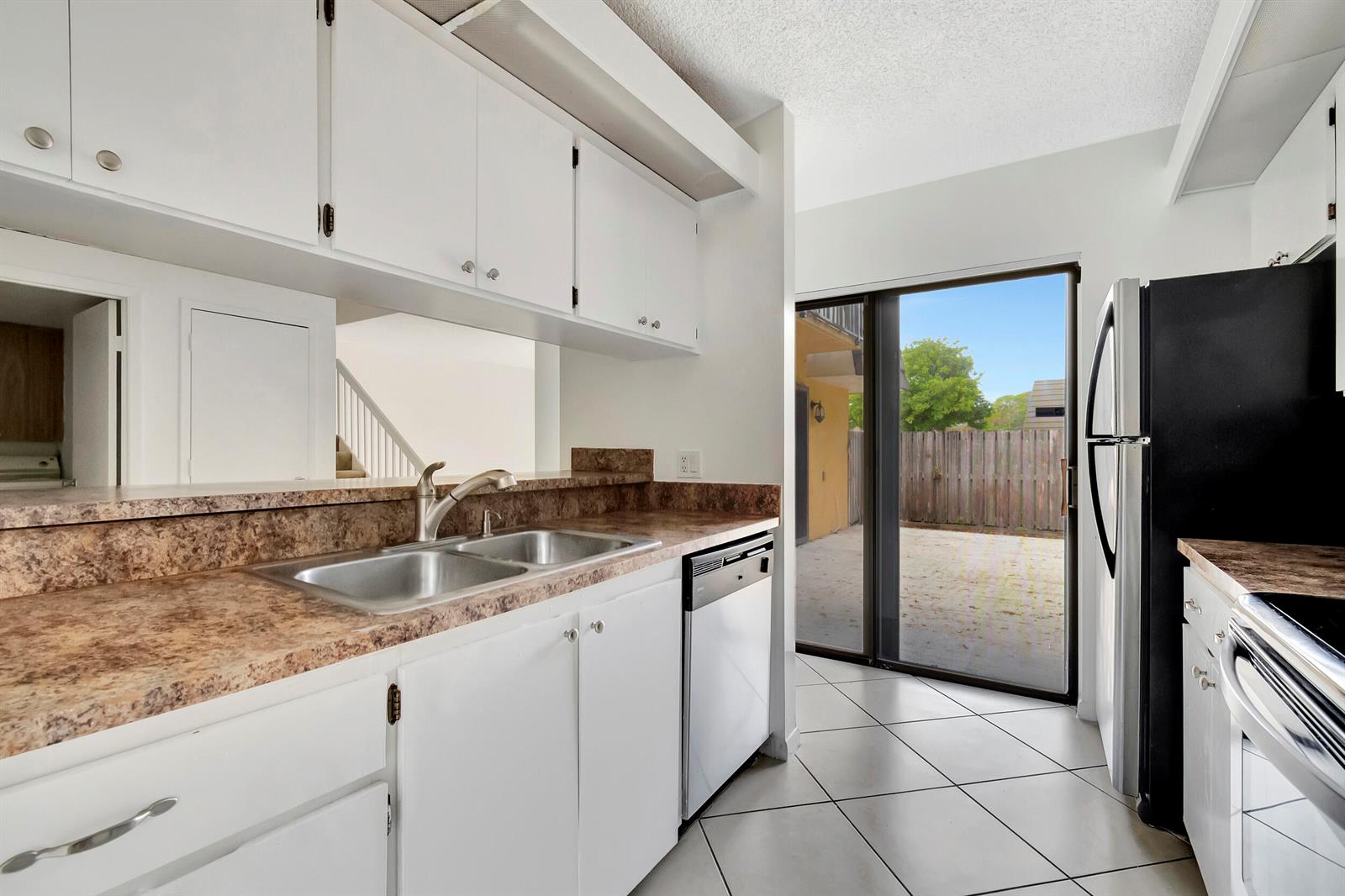 A kitchen with white cabinets, brown laminate countertops, a double sink, and a sliding glass door — 311 3rd Way, West Palm Beach FL 33407, WEST PALM BEACH, FL