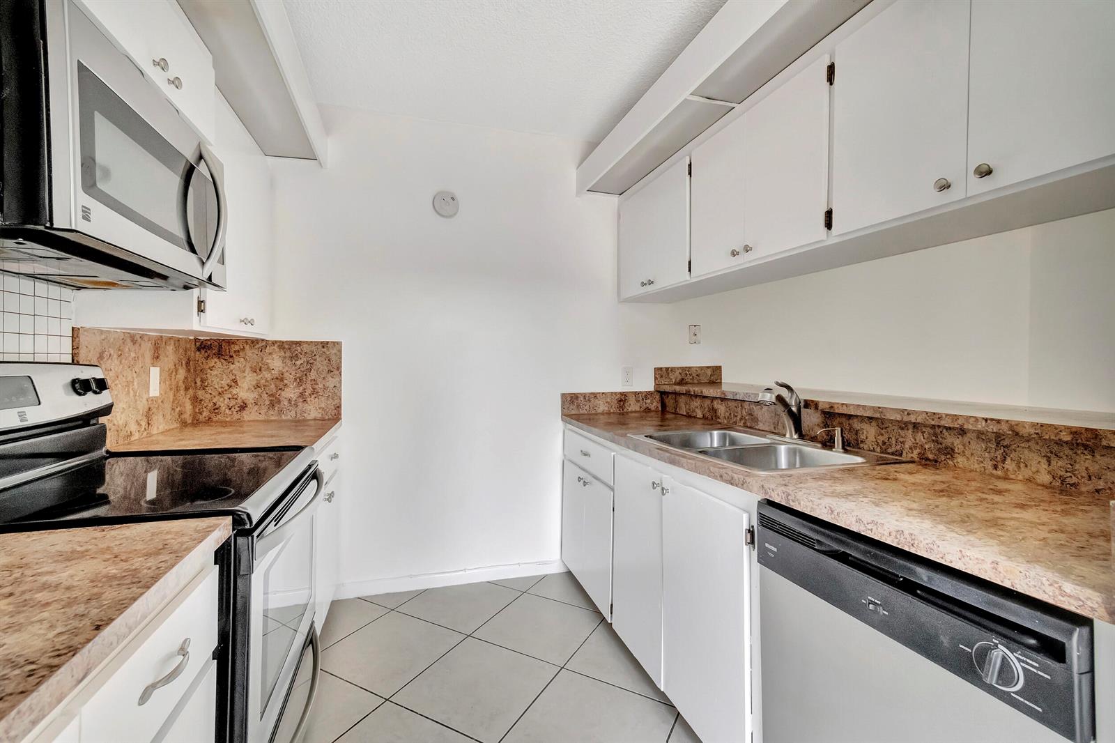 A galley kitchen with white cabinets, brown laminate countertops, and stainless steel appliances — 311 3rd Way, West Palm Beach FL 33407, WEST PALM BEACH, FL