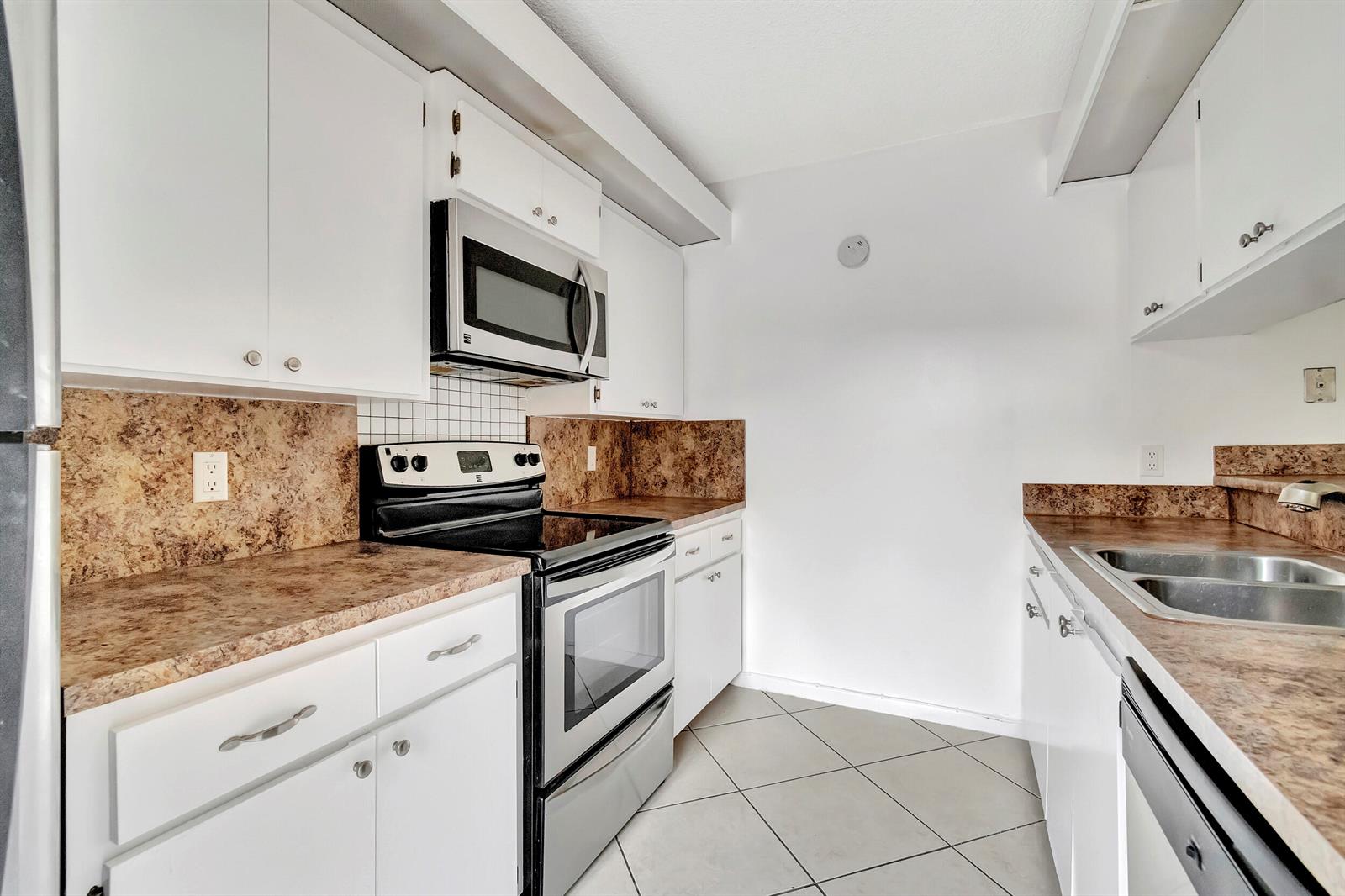 A galley kitchen features white cabinets, brown laminate countertops, stainless steel appliances, and tile flooring — 311 3rd Way, West Palm Beach FL 33407, WEST PALM BEACH, FL