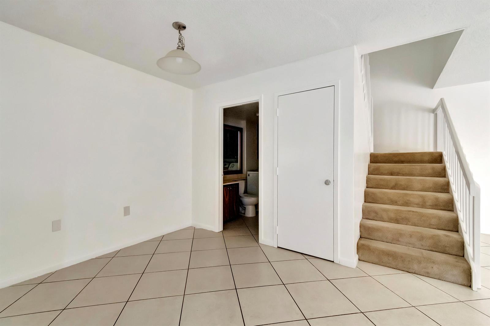 An interior view shows a tiled room with a bathroom doorway, a closet, and carpeted stairs — 311 3rd Way, West Palm Beach FL 33407, WEST PALM BEACH, FL