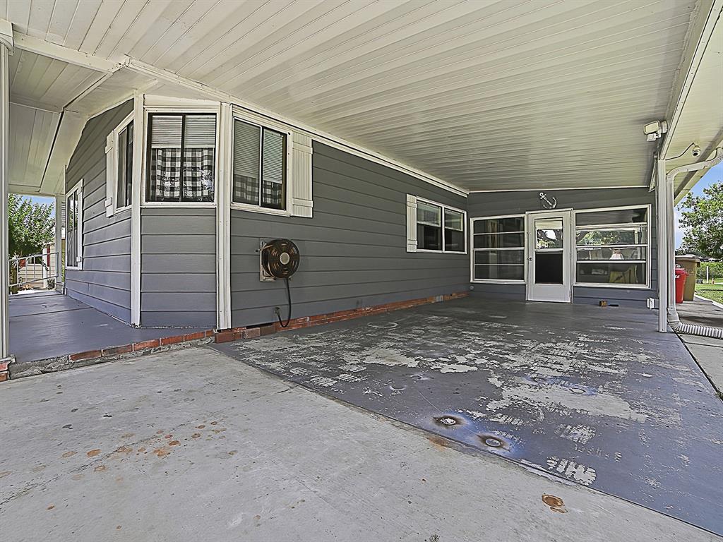 A gray house exterior features a covered concrete carport with peeling paint and brick trim — 25035 BELLEVUE, LEESBURG, FL