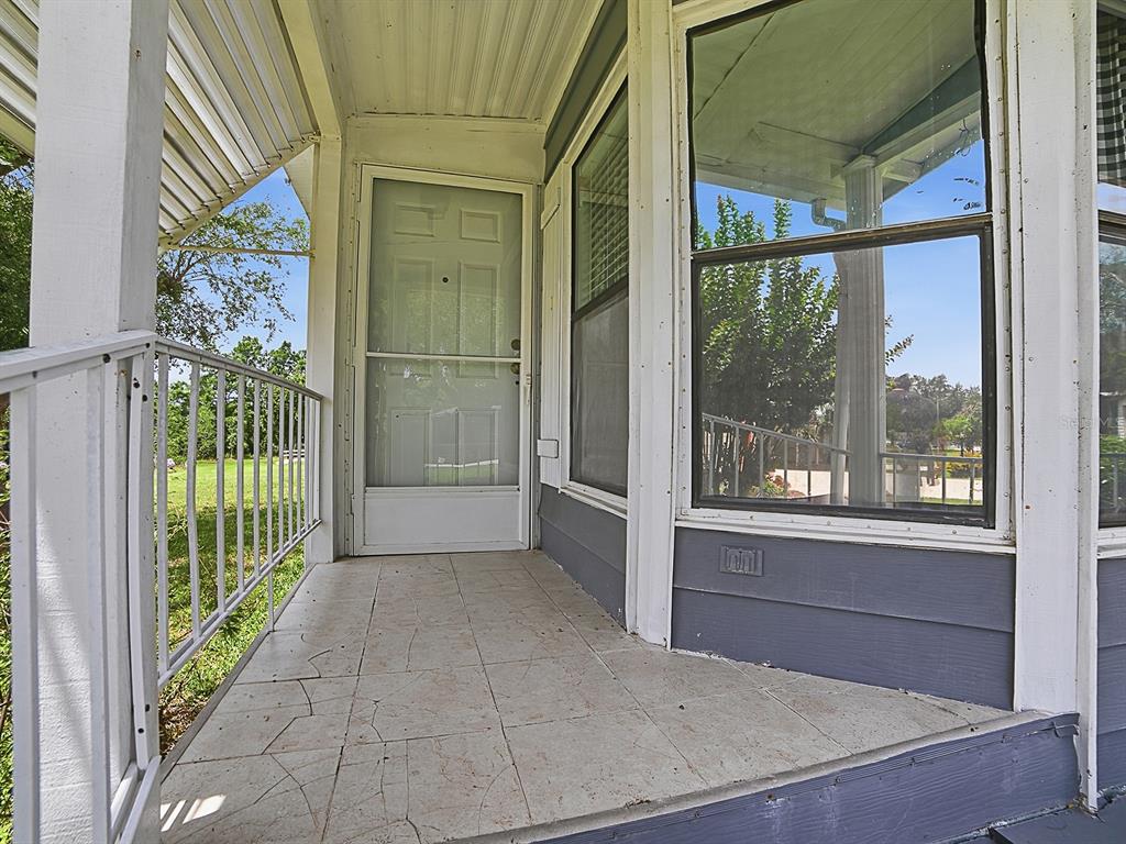 A covered front porch features a tiled floor, a white storm door, and metal railings — 25035 BELLEVUE, LEESBURG, FL