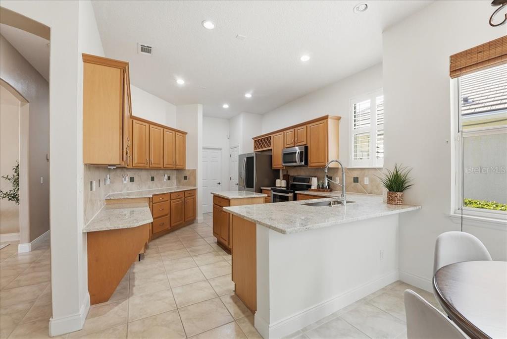 A kitchen features light wood cabinets, granite countertops, tile flooring, and a central island — 10926 WOODCHASE CIRCLE, ORLANDO, FL