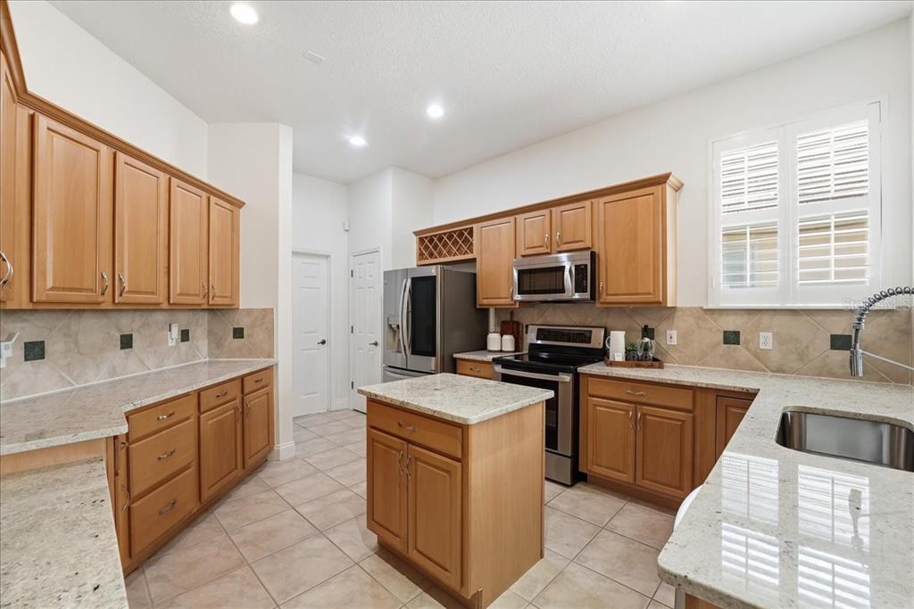 A kitchen features light wood cabinets, granite countertops, stainless steel appliances, and a central island — 10926 WOODCHASE CIRCLE, ORLANDO, FL