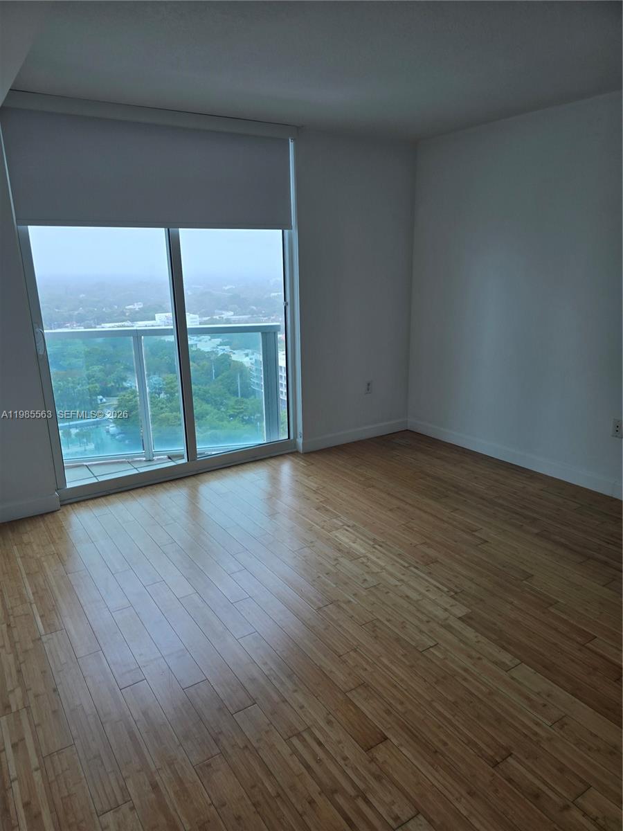 An empty room features light wood flooring, white walls, and a sliding glass balcony door — 2101 Brickell Ave # 1911, Miami FL 33129, MIAMI, FL