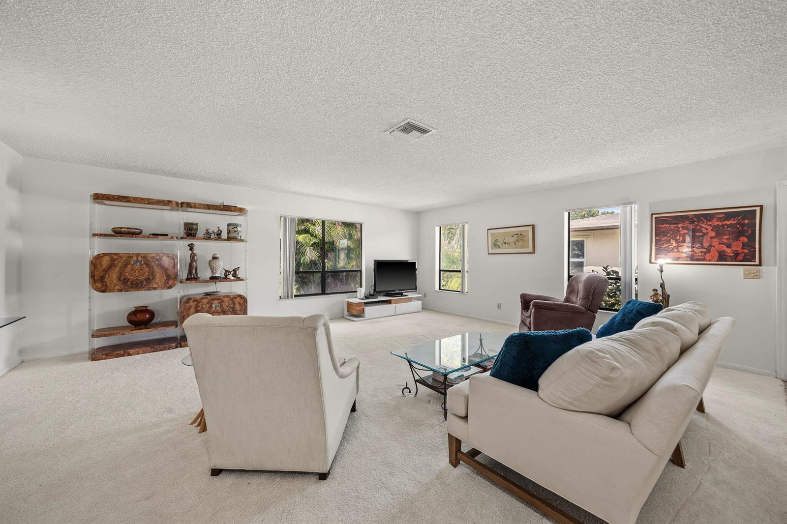 A spacious living room with white walls, beige carpeting, a sofa, armchairs, and shelving units — 7543 Volley Place, Lake Worth FL 33467, LAKE WORTH, FL