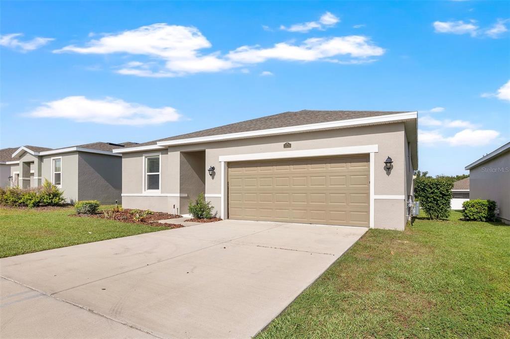 A single-story house with a beige stucco exterior, a two-car garage, and a concrete driveway — 3526 FORSTER AVENUE, LEESBURG, FL