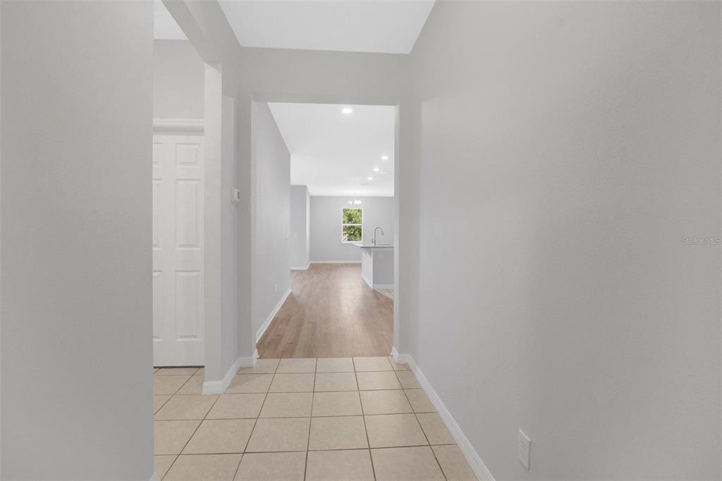 A tiled entryway leads into a hallway with wood-look flooring and a distant kitchen — 3526 FORSTER AVENUE, LEESBURG, FL