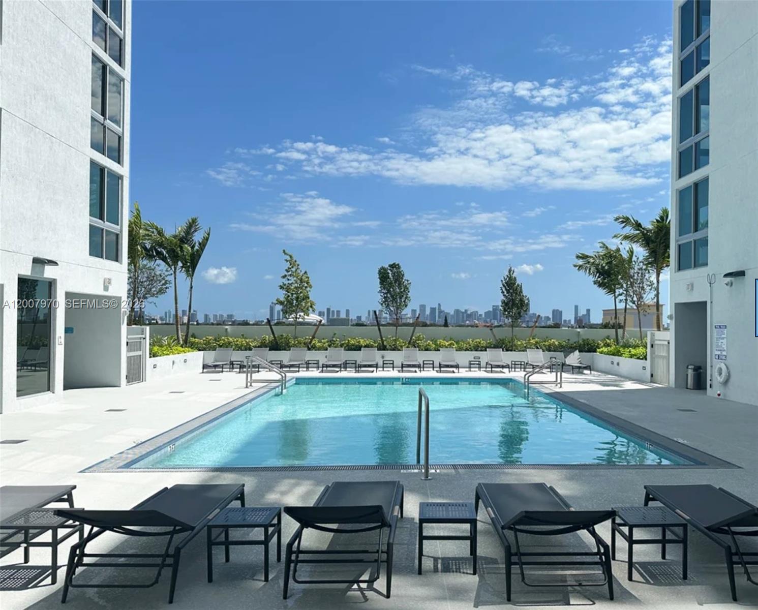 An outdoor swimming pool is surrounded by lounge chairs between two modern white buildings — 61 NW 37th Ave # 01, Miami FL 33125, MIAMI, FL