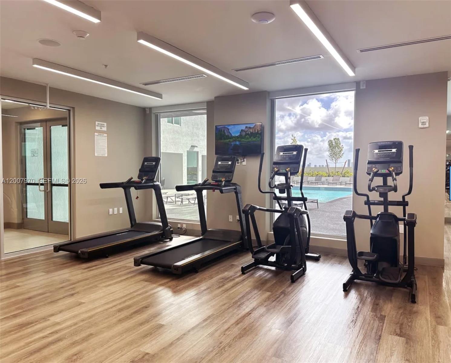 A fitness room features two treadmills and two elliptical machines facing a pool view — 61 NW 37th Ave # 01, Miami FL 33125, MIAMI, FL