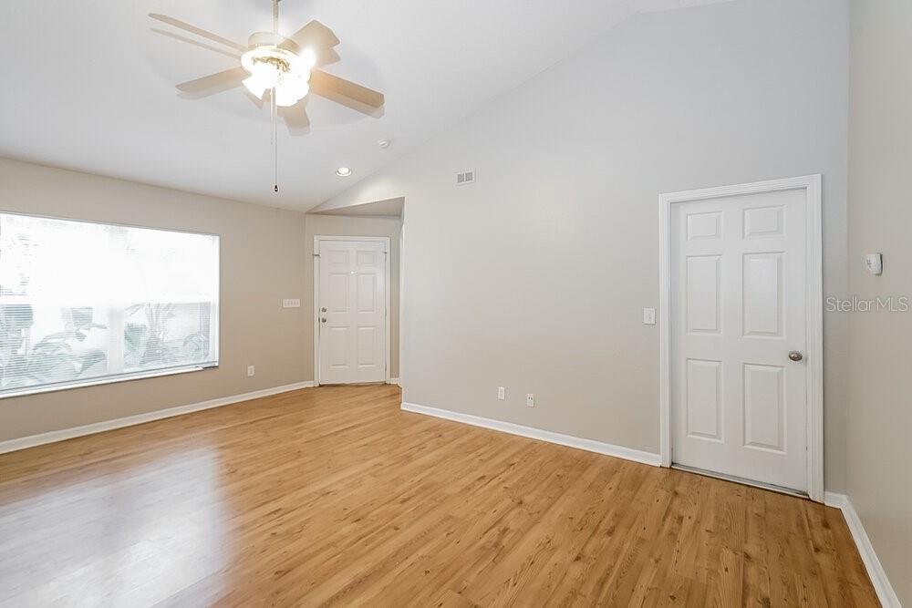 An empty room features light wood flooring, beige walls, a ceiling fan, and two doors — 7445 OXFORD GARDEN CIRCLE, APOLLO BEACH, FL