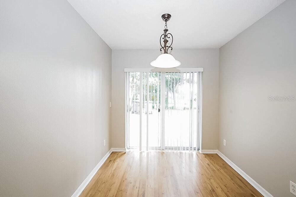 A dining area with light-colored walls, wood-look flooring, a hanging light fixture, and sliding doors — 7445 OXFORD GARDEN CIRCLE, APOLLO BEACH, FL