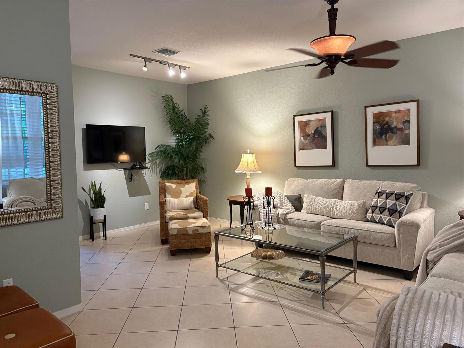 A living room with light green walls, tile flooring, a beige sofa, and a wicker chair — 188 W Thatch Palm Circle, Jupiter FL 33458, JUPITER, FL