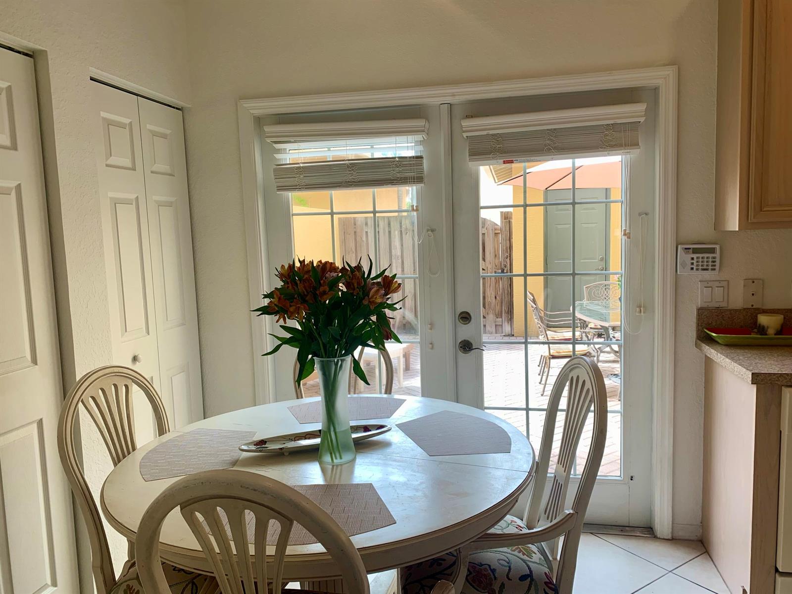 A dining area features a round table with chairs and a vase of flowers before patio doors — 188 W Thatch Palm Circle, Jupiter FL 33458, JUPITER, FL