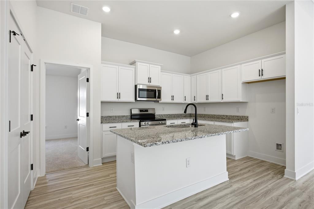 A kitchen with white cabinets, granite countertops, a center island, and light wood-look flooring — 13711 NW 150TH CIRCLE, ALACHUA, FL