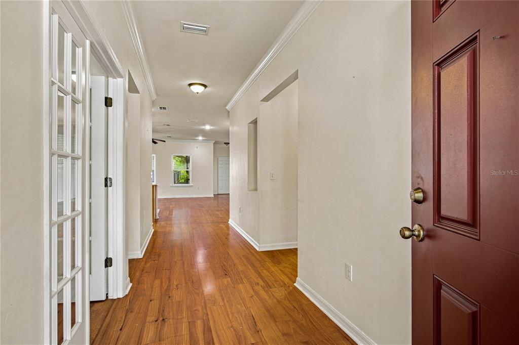 A hallway with hardwood floors leads from a red front door toward an open room — 7654 SW 79TH DRIVE, GAINESVILLE, FL