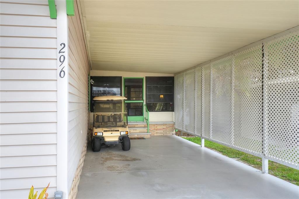 A beige golf cart is parked under a covered carport next to a house entrance — 2055 S FLORAL AVENUE UNIT 296, BARTOW, FL