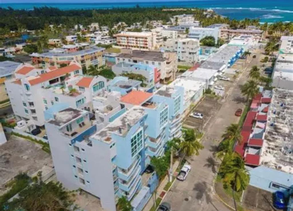 An aerial view shows a multi-story blue apartment complex near a coastal beach area — 306 OCEAN WALK CHALETS, LUQUILLO, PR