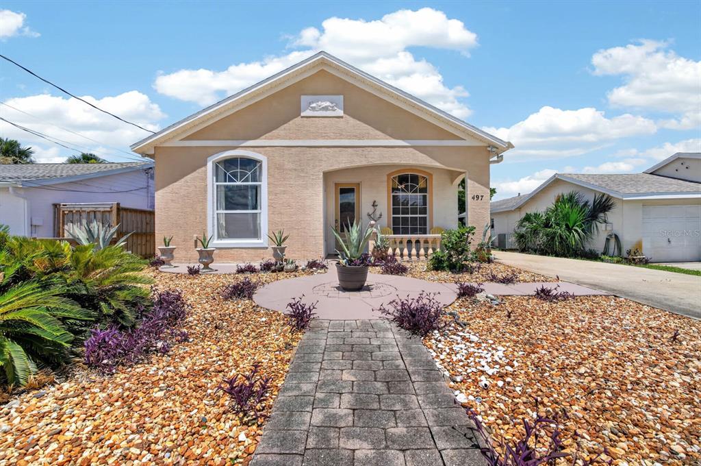 A single-story house with a beige stucco exterior, a stone walkway, and a rock-covered yard — 497 GRANDVIEW AVENUE, ORMOND BEACH, FL
