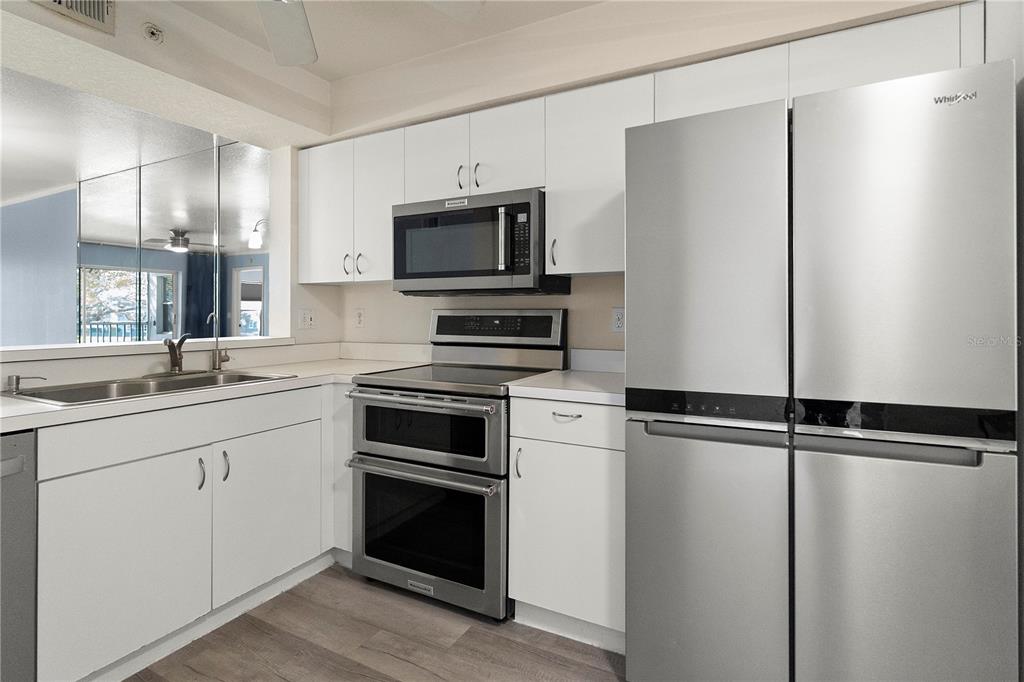 A kitchen features white cabinets, stainless steel appliances, and light wood-look flooring — 9610 VICTORIA LANE UNIT D202, NAPLES, FL