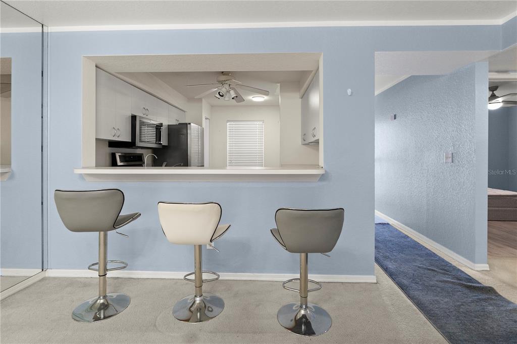 A kitchen pass-through window overlooks a breakfast bar with three stools in a living area — 9610 VICTORIA LANE UNIT D202, NAPLES, FL