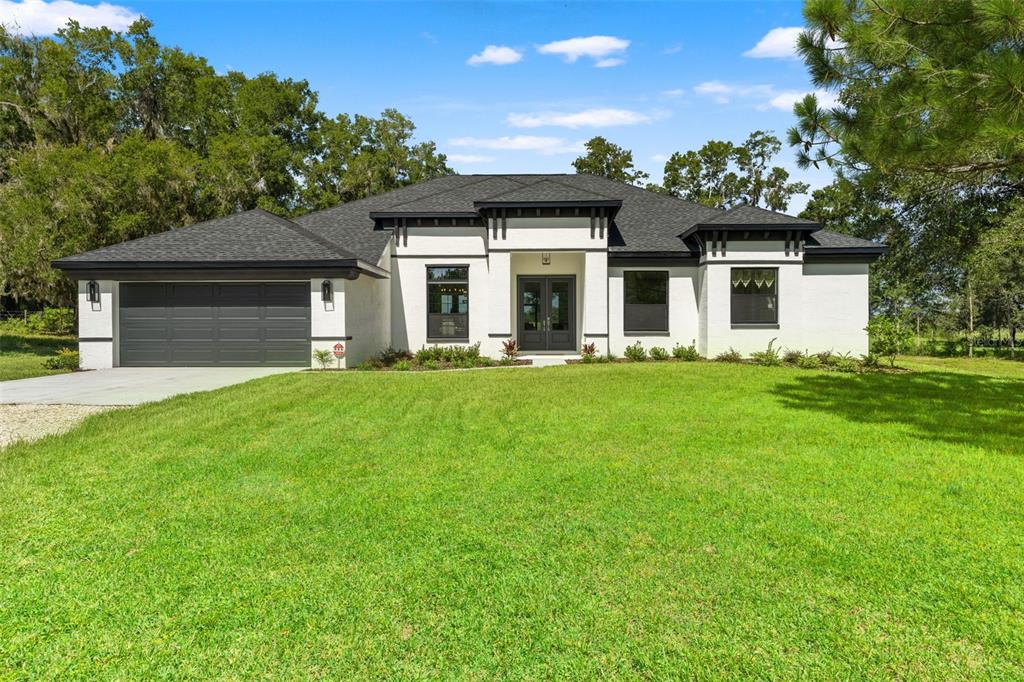 A single-story white house with a dark roof and garage sits on a grassy lawn — 10264 S LECANTO HIGHWAY, LECANTO, FL
