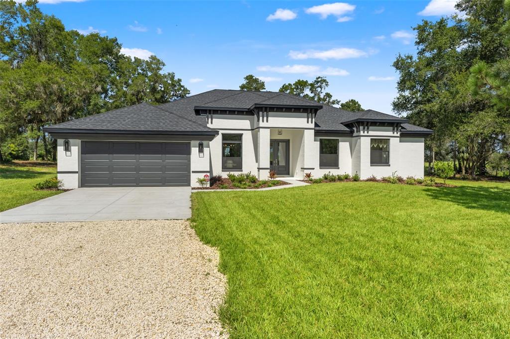A single-story white house with a dark roof and a two-car garage sits on grass — 10264 S LECANTO HIGHWAY, LECANTO, FL