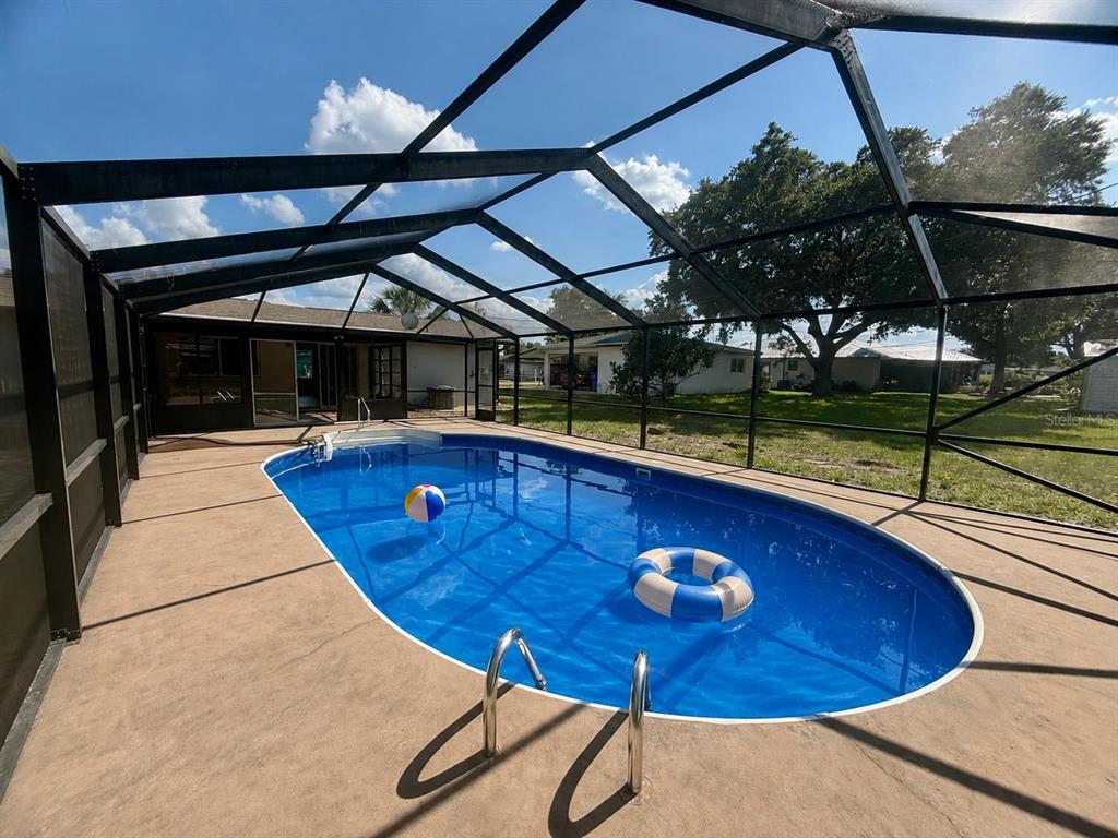 An oval swimming pool sits inside a screened-in patio enclosure behind a residential home — 131 SPARROW AVENUE, SEBRING, FL