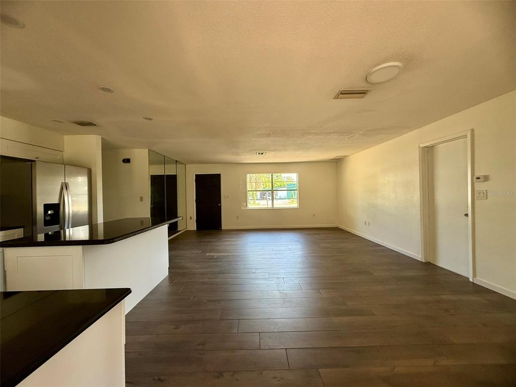 An open-concept living area features wood-look tile flooring and a kitchen with black countertops — 131 SPARROW AVENUE, SEBRING, FL