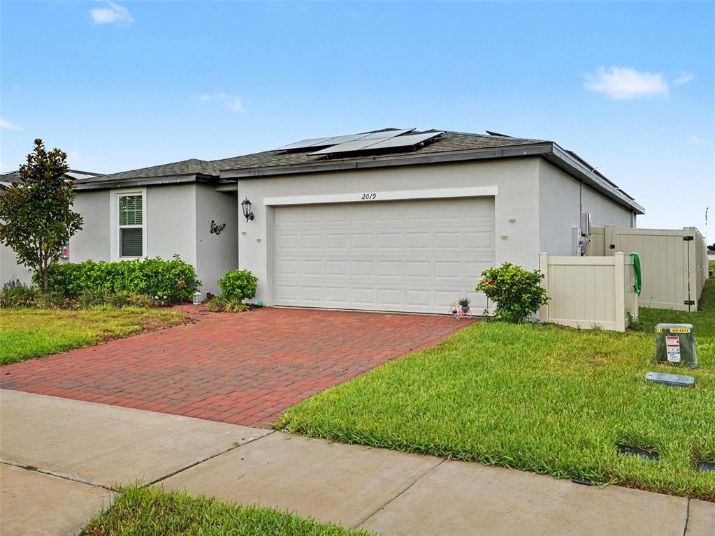 A backyard features a concrete patio, artificial turf, red pavers, and a tan house exterior — 2019 KINGSMEN COURT, HAINES CITY, FL