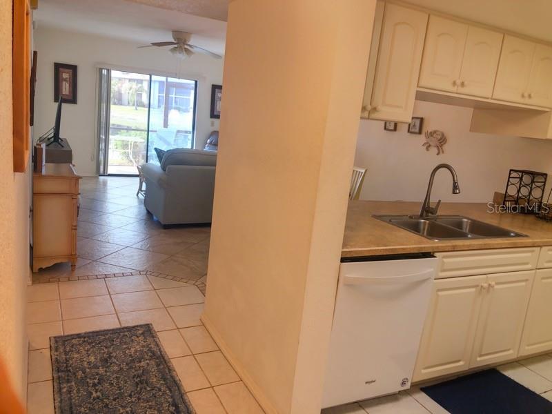 A kitchen with white cabinets and a dishwasher opens into a living area with tile floors — 4024 OAKVIEW DRIVE UNIT I3, PUNTA GORDA, FL