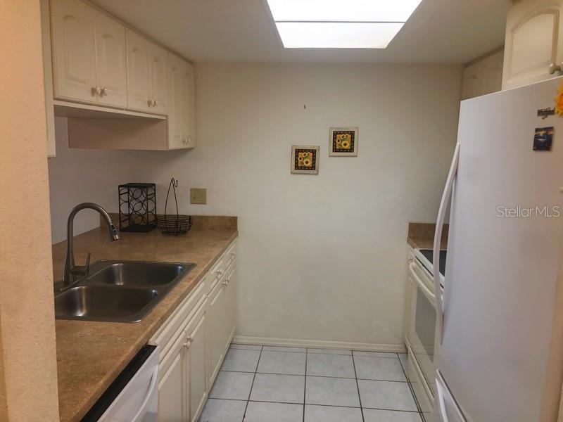 A galley kitchen features white cabinets, tan countertops, a double sink, and white appliances — 4024 OAKVIEW DRIVE UNIT I3, PUNTA GORDA, FL