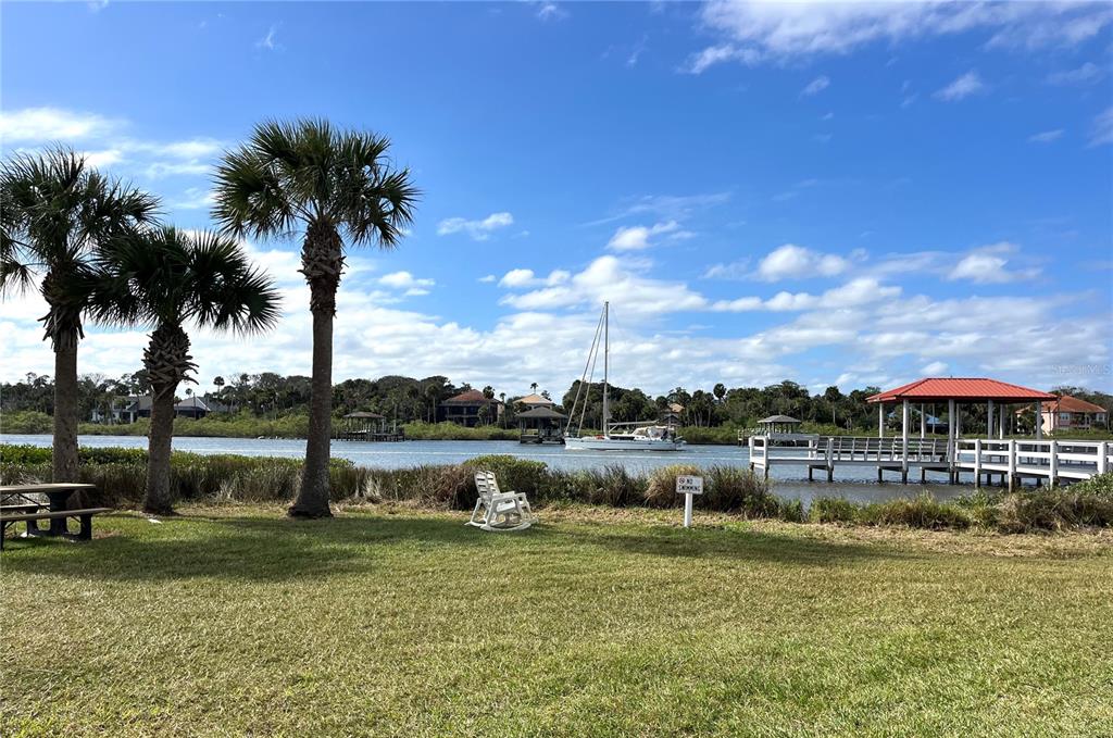A grassy lawn overlooks a waterway with a sailboat, a dock, and palm trees — 169 LOOKOUT DRIVE, FLAGLER BEACH, FL