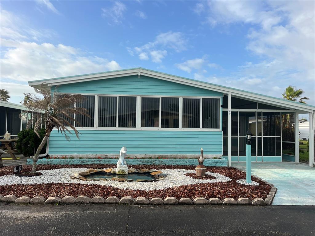 A light blue mobile home features a front pond, a screened porch, and white trim — 169 LOOKOUT DRIVE, FLAGLER BEACH, FL