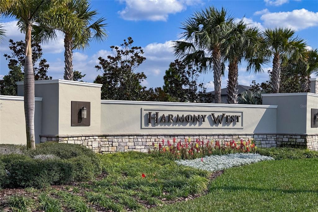 A stone and stucco monument sign for Harmony West stands among palm trees and landscaping — 2653 HARMONIA HAMMOCK ROAD, HARMONY, FL