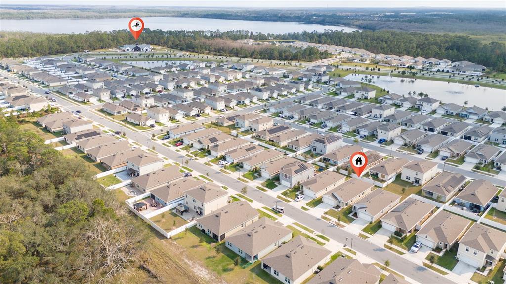 An aerial view shows a suburban neighborhood with many houses, a lake, and wooded areas — 2653 HARMONIA HAMMOCK ROAD, HARMONY, FL