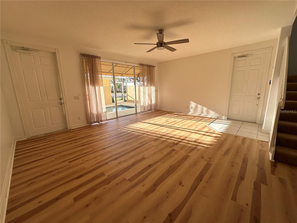 An empty living room features light wood flooring, a ceiling fan, and sliding glass patio doors — 7776 ANDORA DRIVE, SARASOTA, FL