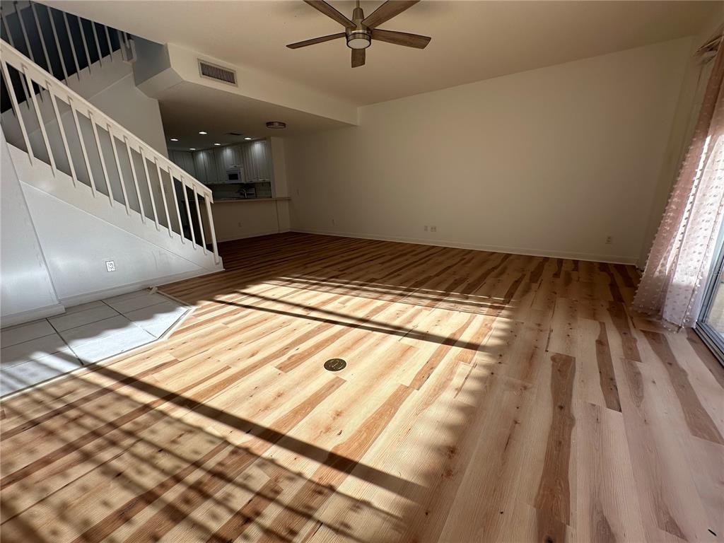 An open living area features light wood flooring, a staircase with white railings, and a kitchen — 7776 ANDORA DRIVE, SARASOTA, FL