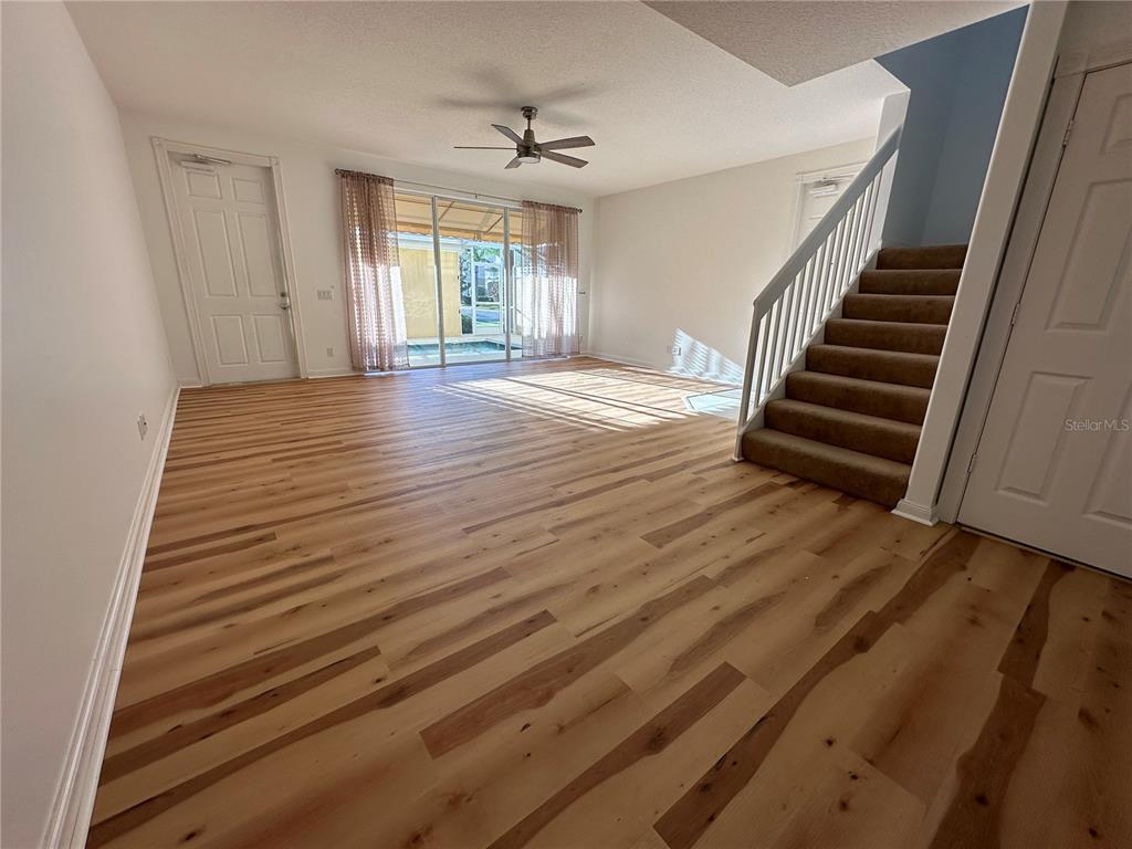 An empty living room features light wood-look flooring, a ceiling fan, and a carpeted staircase — 7776 ANDORA DRIVE, SARASOTA, FL