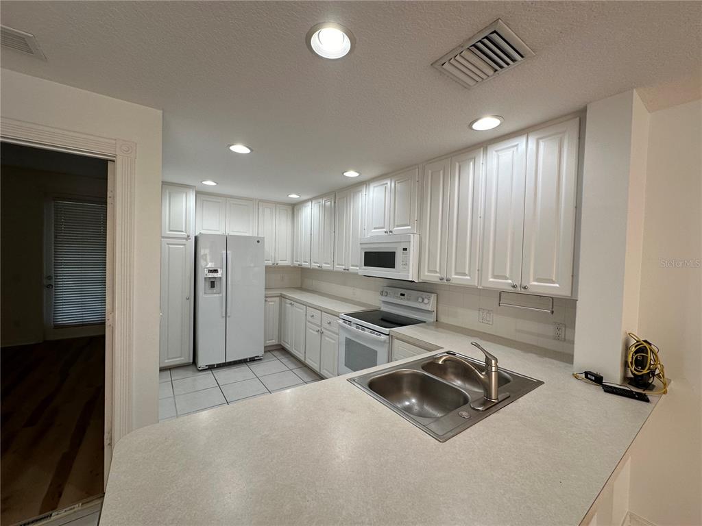 A kitchen features white cabinetry, white appliances, a double-basin sink, and light-colored countertops — 7776 ANDORA DRIVE, SARASOTA, FL