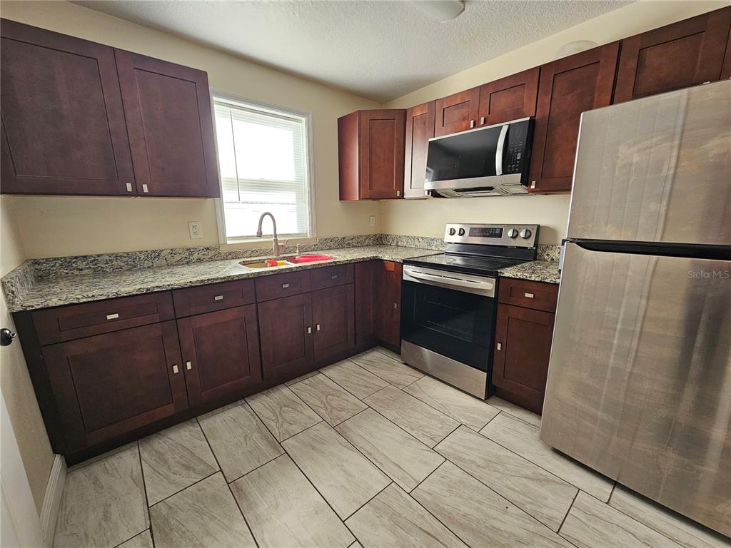 A kitchen features dark wood cabinets, granite countertops, stainless steel appliances, and light tile flooring — 701 N 7TH ST, HAINES CITY, FL