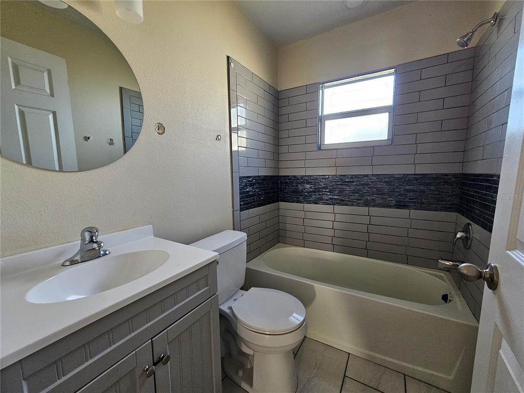 A bathroom features a gray vanity, a round mirror, a toilet, and a tiled tub-shower — 701 N 7TH ST, HAINES CITY, FL