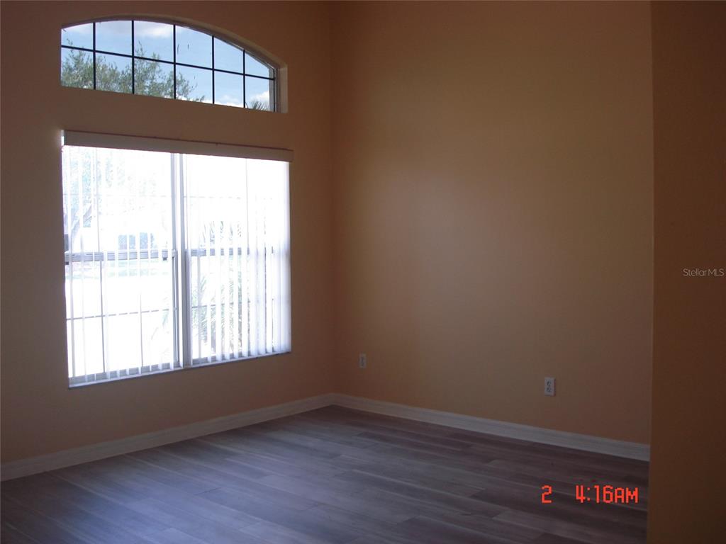 An empty room features light-colored wood-look flooring, tan walls, and a large arched window — 606 ALDER GROVE DRIVE, DELTONA, FL
