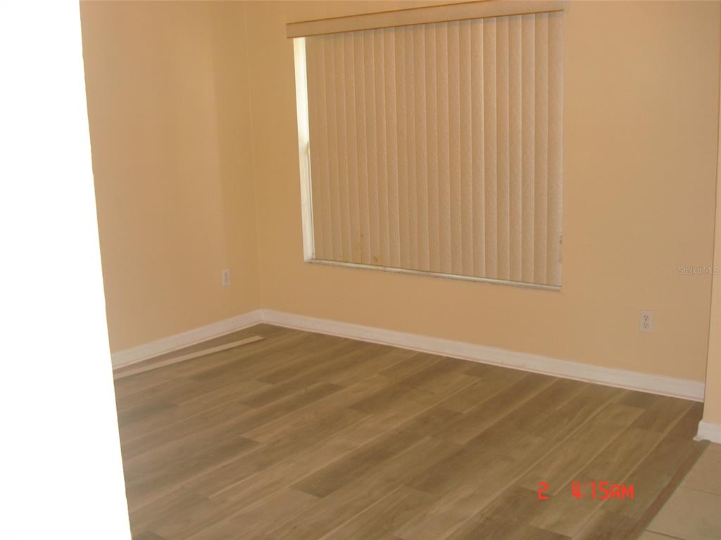 An empty room features light-colored walls, wood-look flooring, and vertical blinds covering a window — 606 ALDER GROVE DRIVE, DELTONA, FL