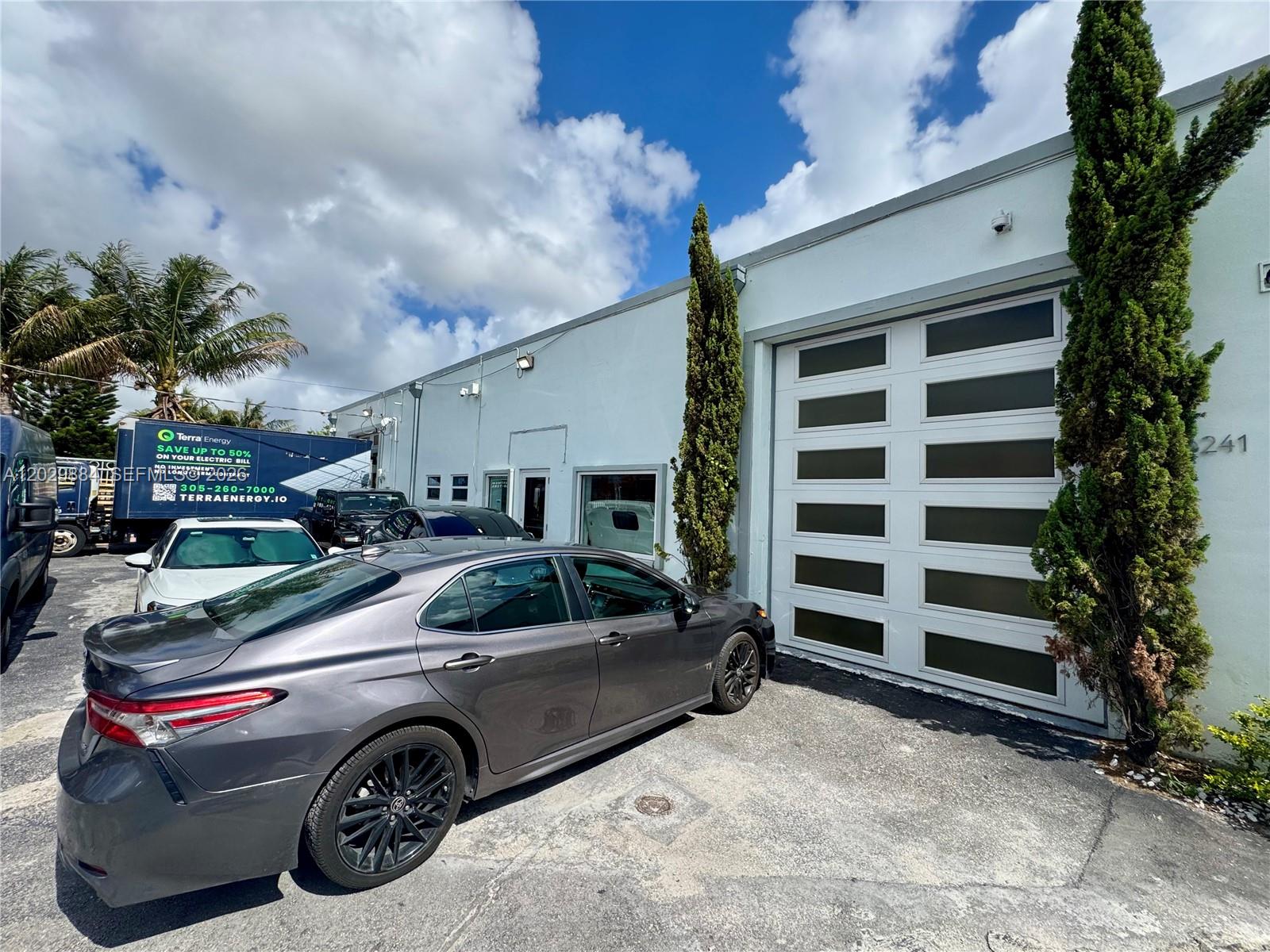 A gray sedan is parked in front of a white commercial building with a garage door — 3241 NW 38th St, Miami FL 33142, MIAMI, FL